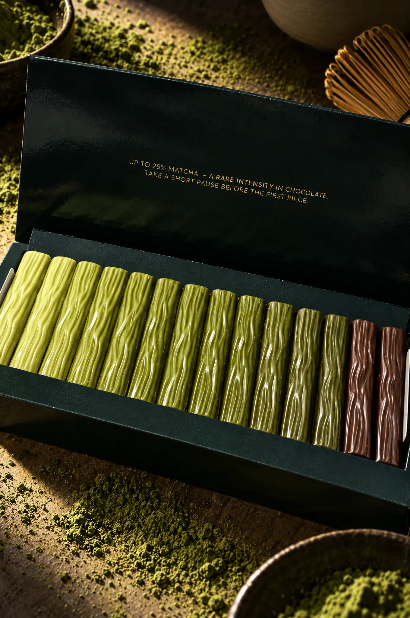 Open box of 7 Shades of Matcha with sticks from light to dark green, matcha powder and a bamboo whisk