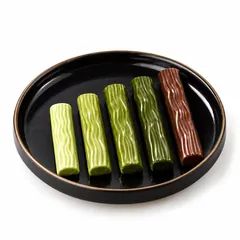 Quattro stick di cioccolato al matcha in sfumature diverse e uno stick all’hojicha su un piatto nero