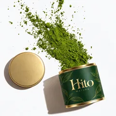 Катурната кутийка Hito Matcha, от която се сипе матча на прах, а до нея е златистият капак